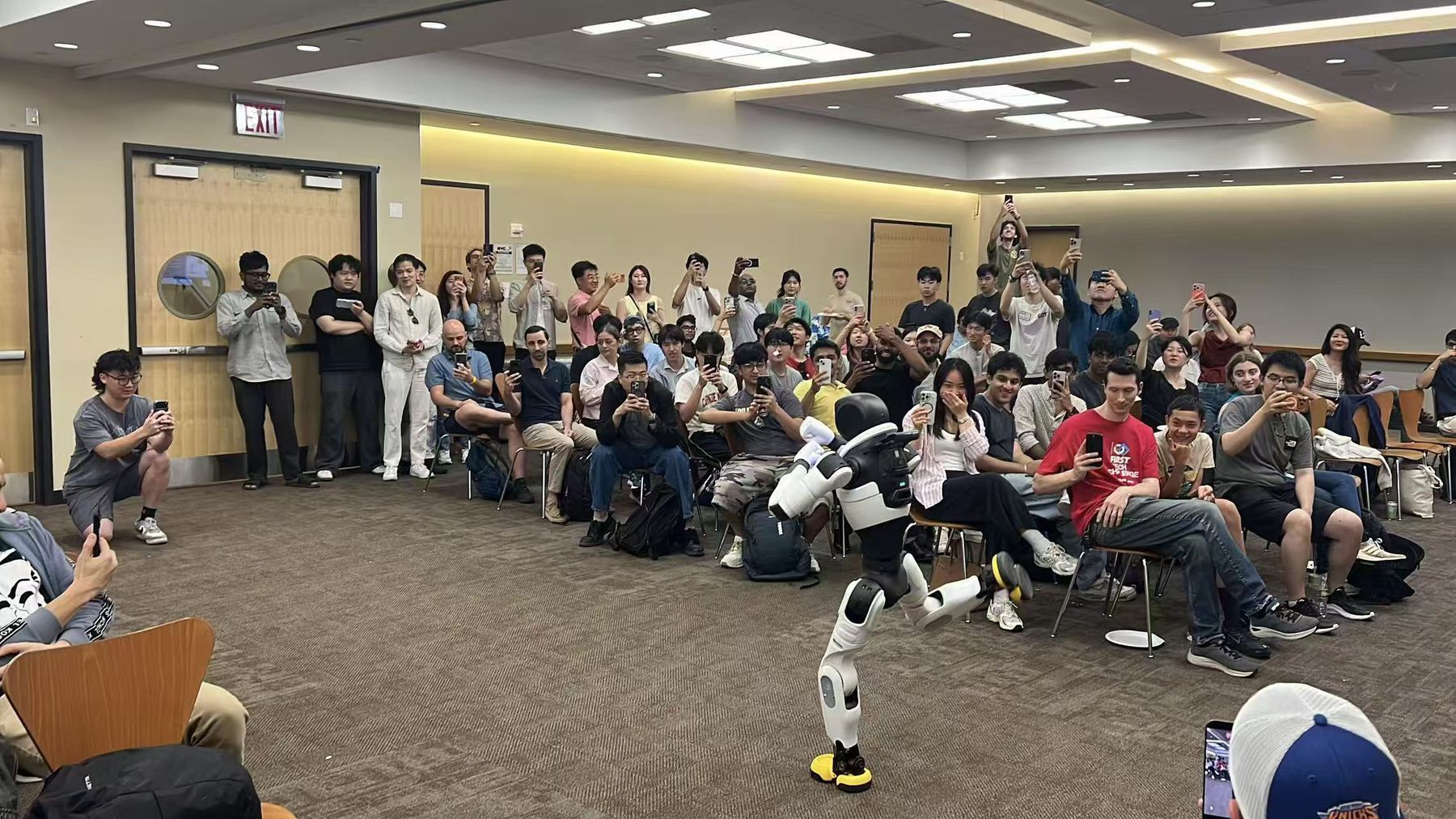 A humanoid robot mid-demonstration in a packed room